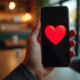 Main avec smartphone affichant un emoji cœur rouge dans un café